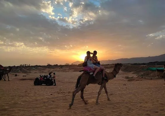 Guests ride camels across the desert at sunset